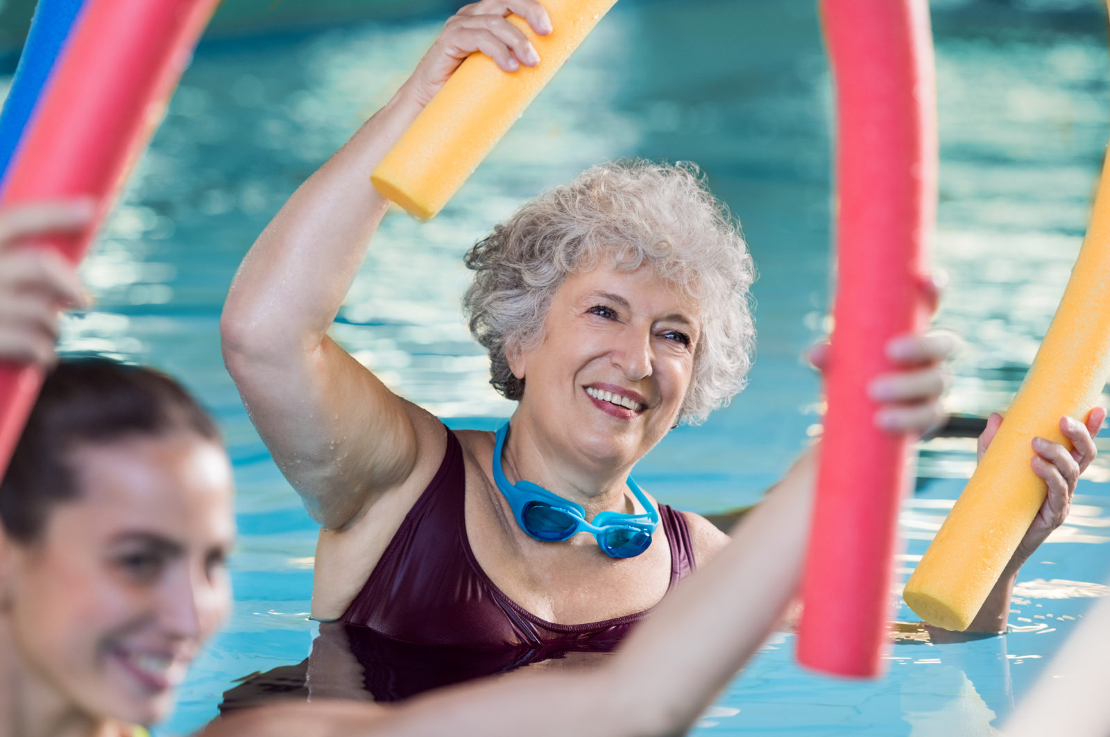 elderly woman in pool doing water aerobics with foam noodles