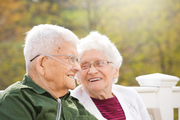 elderly couple sitting outside on a park bench, smiling