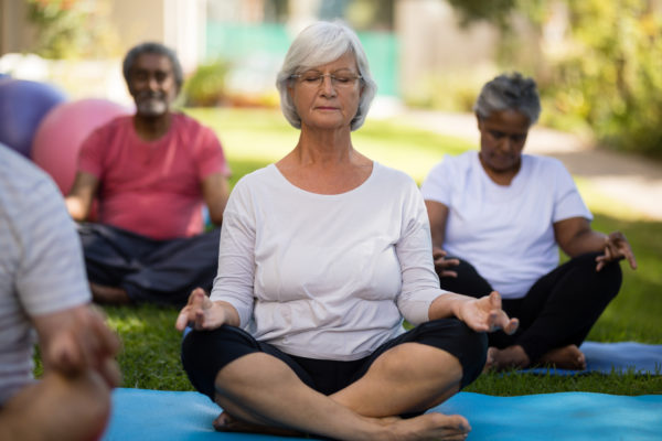 Senior woman meditating with closed eyes while sitting amidst friends at park