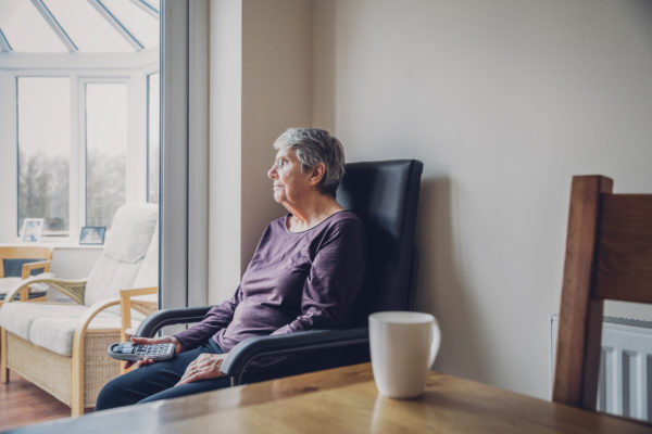 senior woman sitting alone in kitchen holding telephone in her lap;