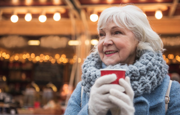 elder woman dressed in warm clothes holding a cup of coffee