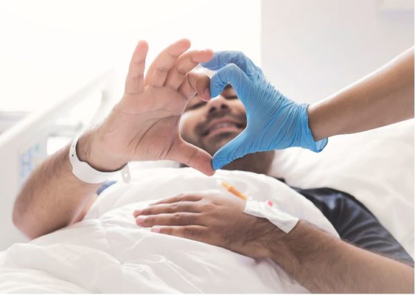 man lying in hospital bed. His right hand and a doctor's hand form a heart shape.