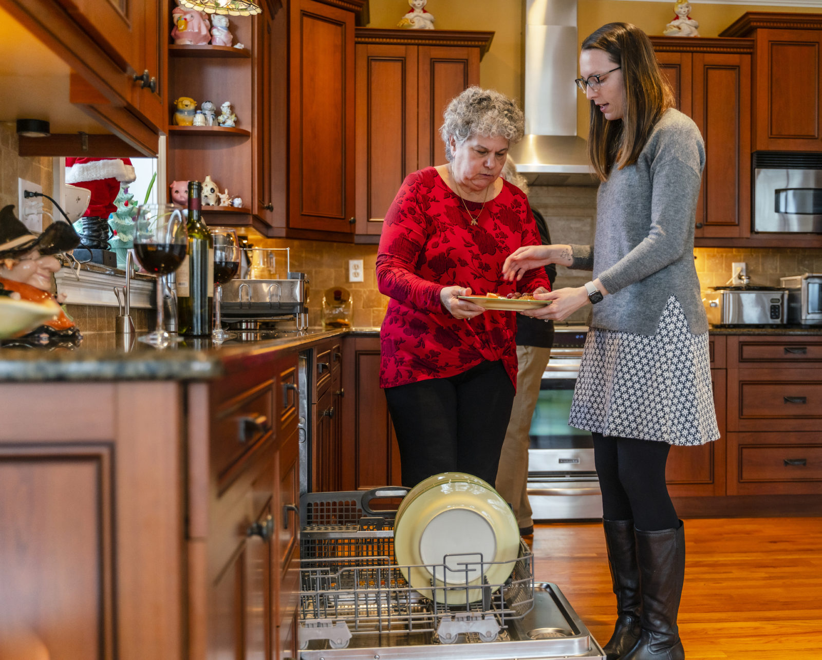 Adult kid visiting their senior parents during the holiday season, helping in the kitchen by placing dirty dishes into the dishwasher