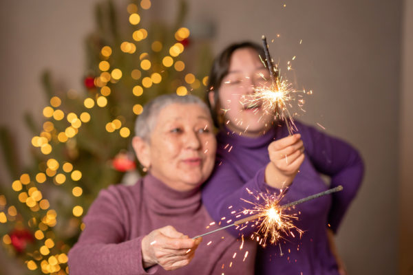 An Asian grandmother and granddaughter burn sparklers in the against the background of a Christmas tree.