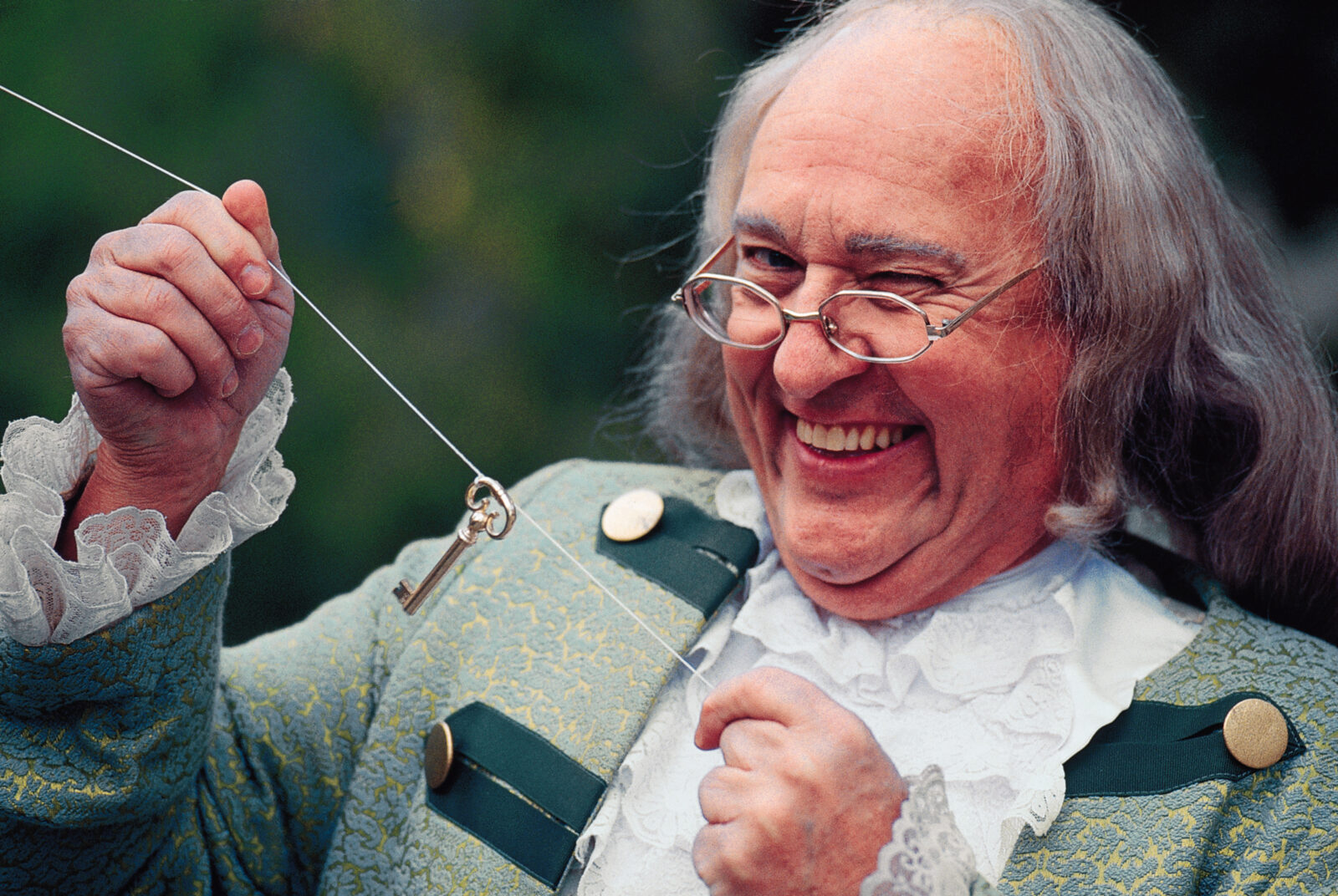 Portrait of man dressed as Benjamin Franklin with key and kite winking at camera