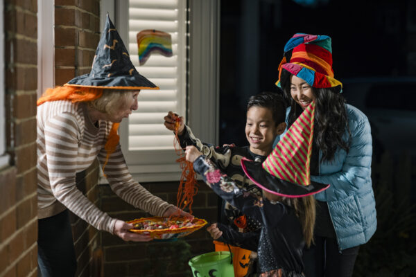 A family wearing fancy dress, out trick or treating in North East England during halloween. They are standing at their neighbours and taking strawberry laces off a a plastic plate that she is holding.