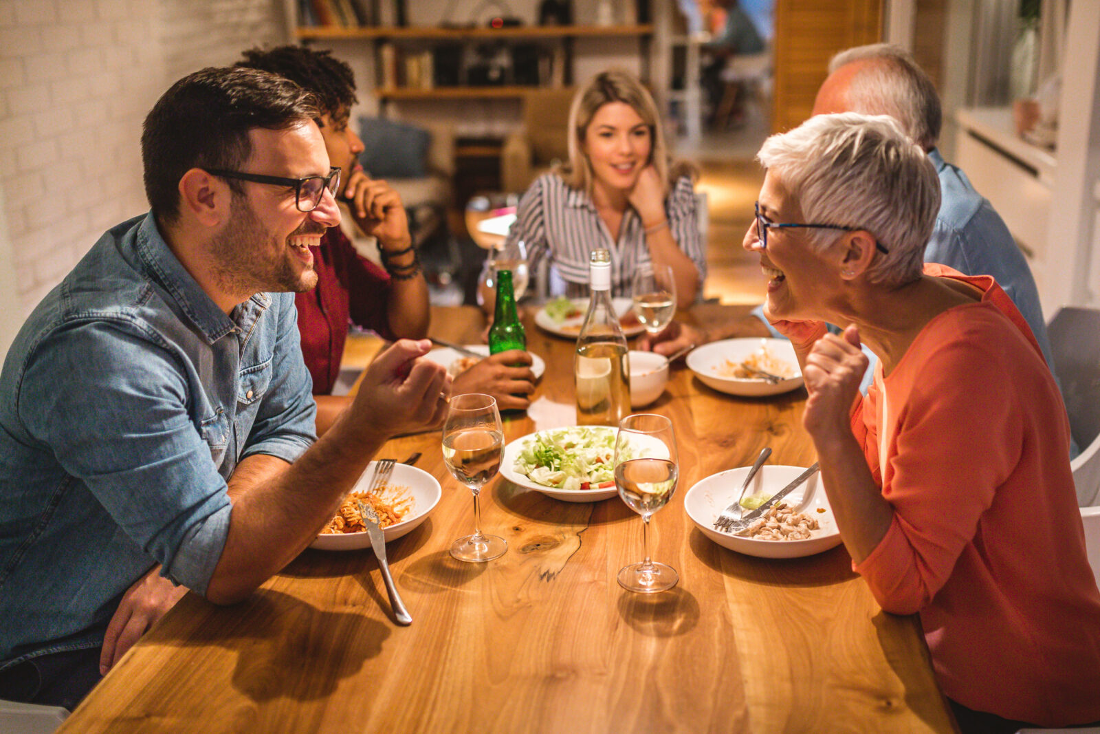 Joyful members of a multiracial family enjoying a holiday dinner. A son is talking with his mother in the foreground.