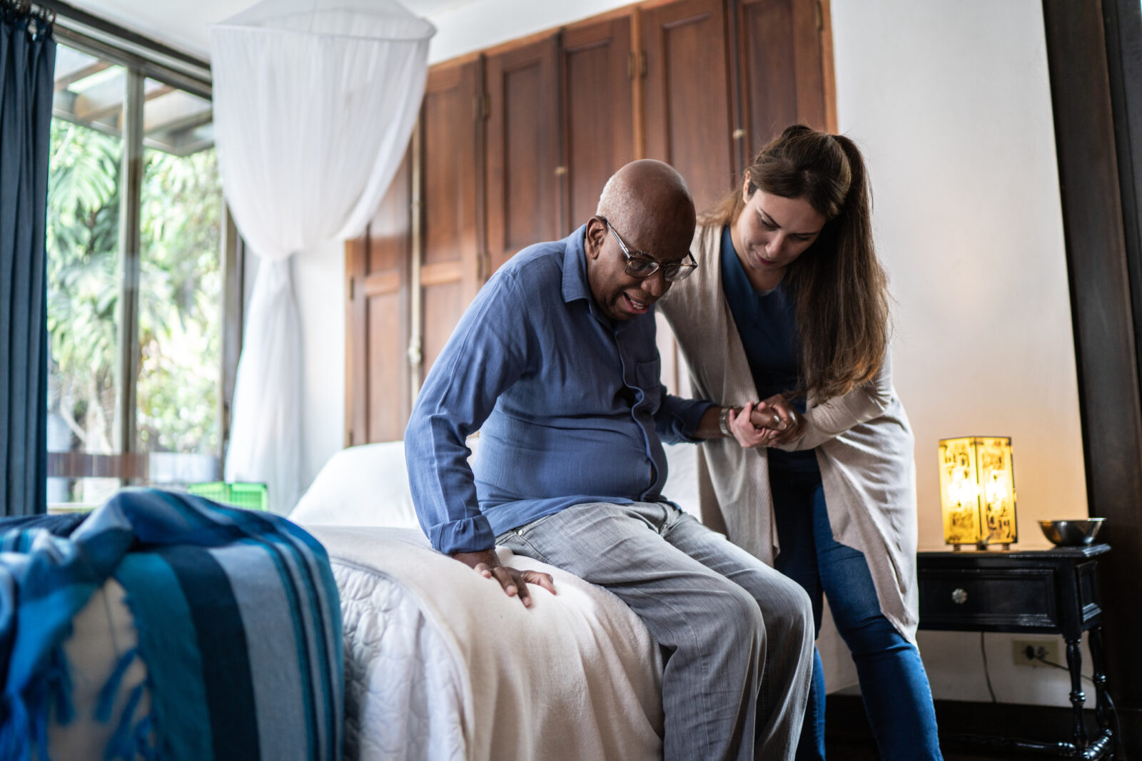 Home caregiver helping a Black senior man standing up at home