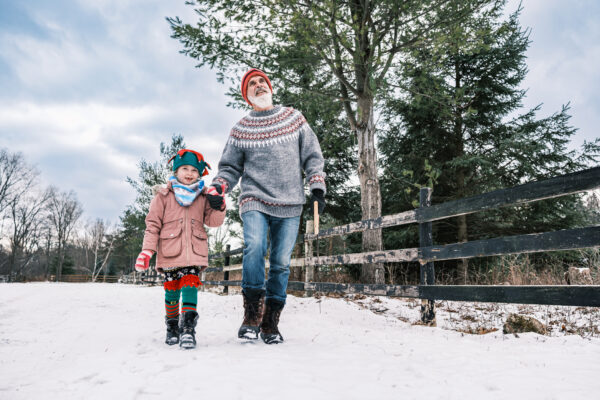 Grandfather and granddaughter dressed in warm winter clothing. walk along a path in the snow with trees.
