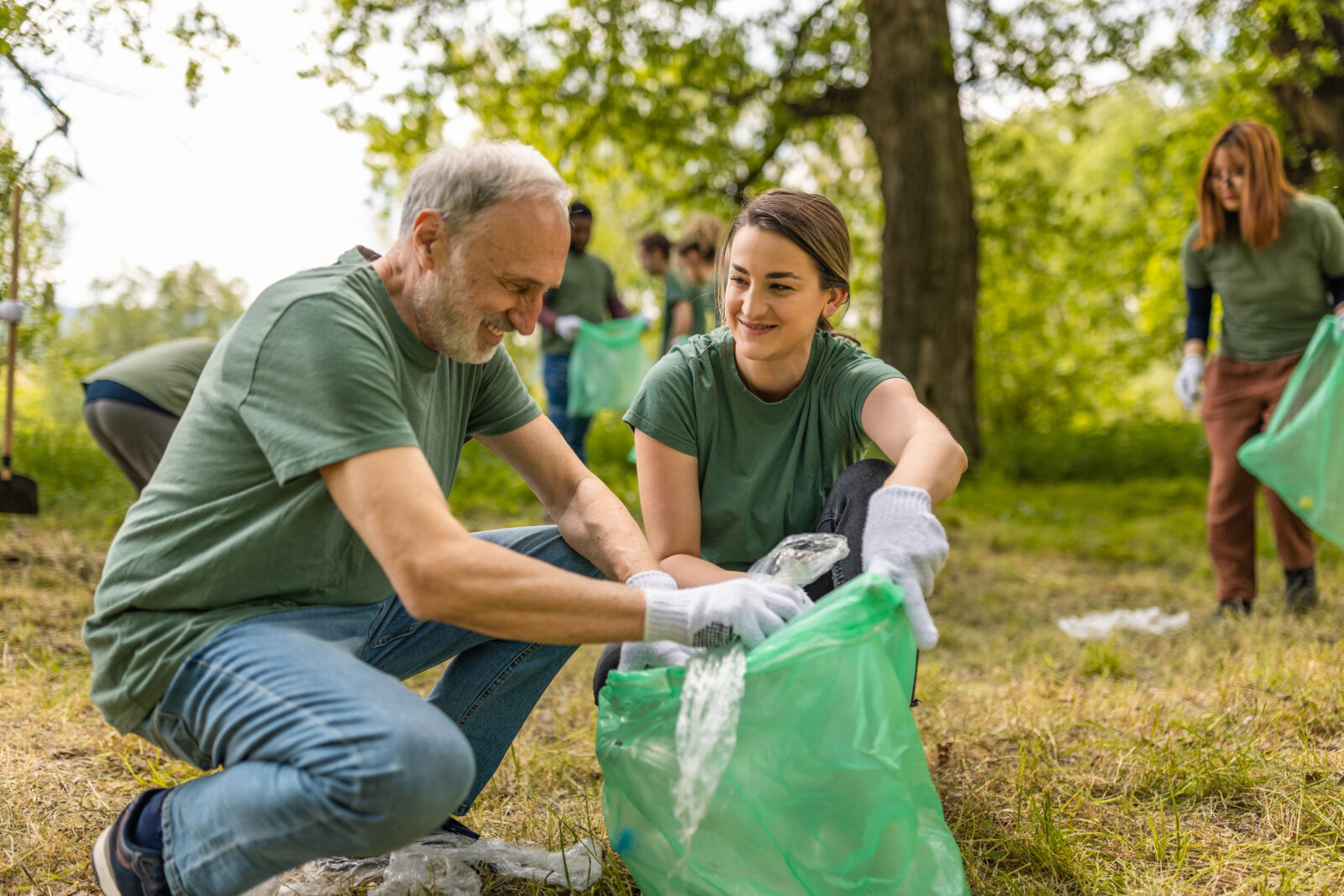 Old man and college-age woman collect trash in a forest together as part of a community volunteer effort.
