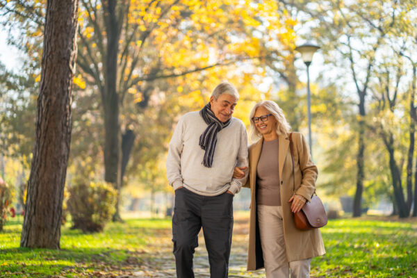 Senior couple walking arm in arm, smiling in an autumn park